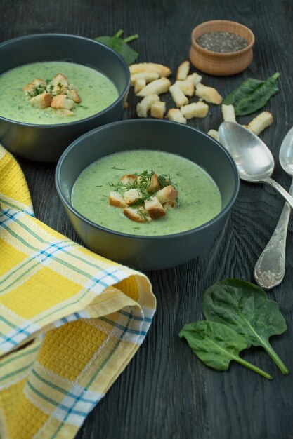 Sopa cremosa de espinafre com bolachas, ervas e sementes de chia. Sopa verde, servido em uma tigela sobre uma mesa de madeira.