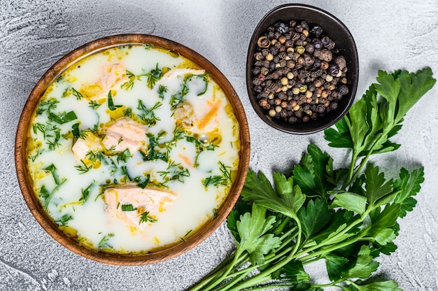 Sopa cremosa de pescado con salmón, trucha, papas y perejil. Fondo gris, vista desde arriba.