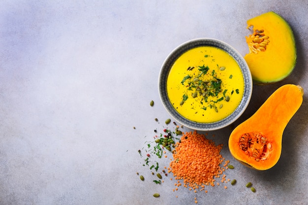 Sopa cremosa de verduras y lentejas, calabaza cortada, semillas, perejil en gris claro.