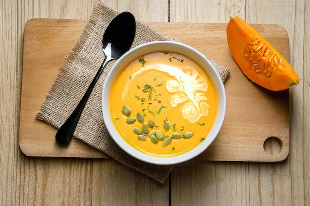 Sopa de abóbora amarela com fatia de abóbora no fundo de madeira vista superior