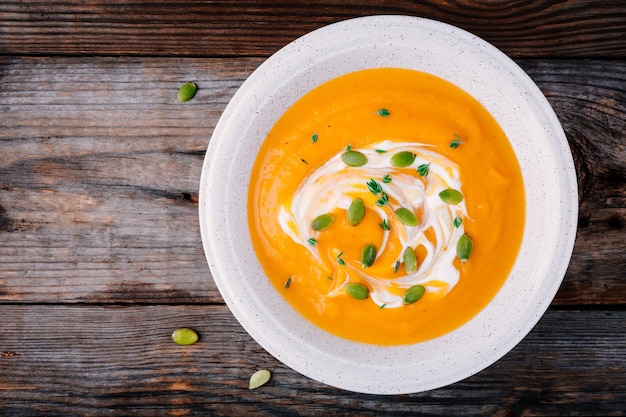 Sopa de abóbora caseira com creme e sementes em fundo de madeira