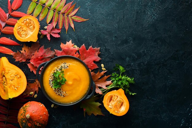 Sopa de abóbora com abóbora e folhas de outono coloridas sobre um fundo de pedra preta Vista superior Espaço livre para o seu texto