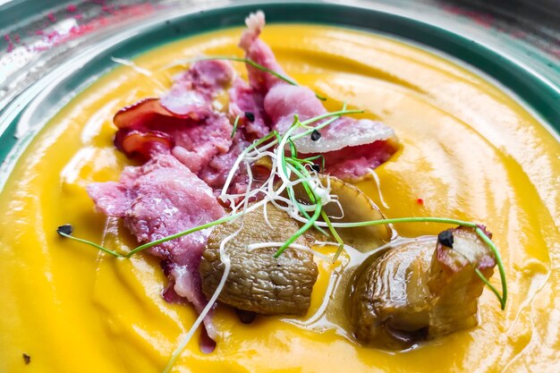 Sopa de abóbora com cogumelos, bacon, microgreen em um prato verde.