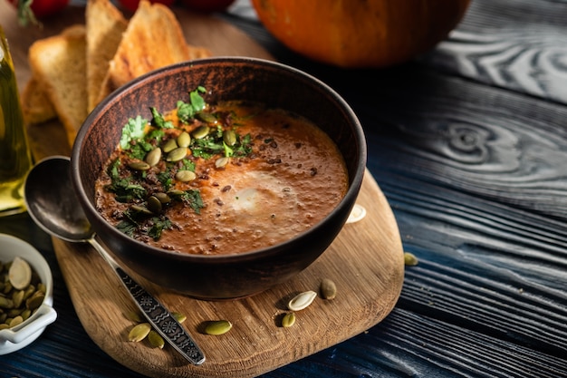 Sopa de abóbora com creme de leite e sementes de abóbora em uma mesa de madeira.