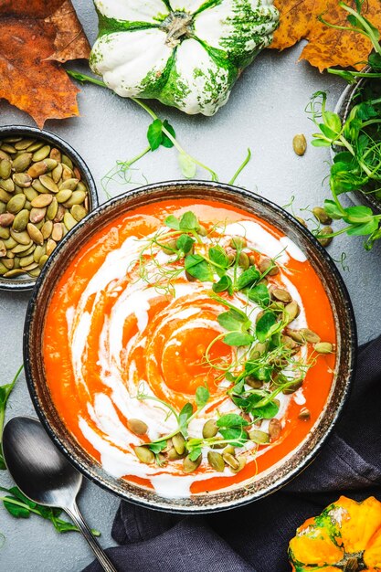 Foto sopa de abóbora com creme de sementes e brotos de ervilha verde inverno ou outono comida lenta saudável tigela de sopa no fundo da mesa cinza vista superior