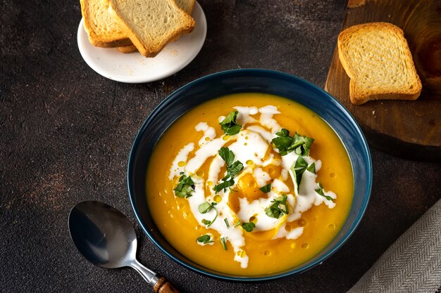 Sopa de abóbora com creme e salsa na mesa rústica escura