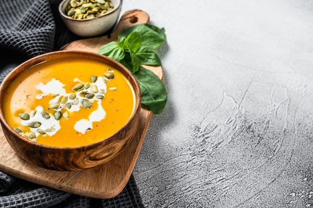 Sopa de abóbora com creme, sementes e manjericão fresco em tigela de madeira rústica. fundo cinza