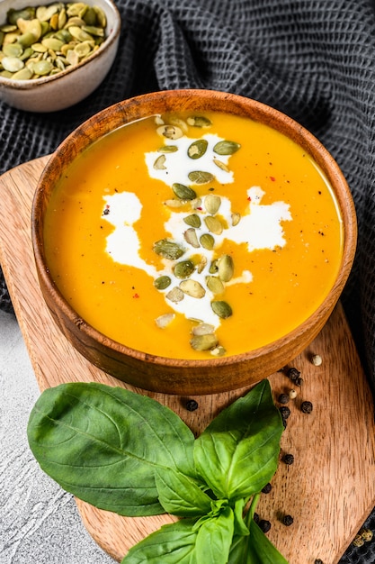 Sopa de abóbora com creme, sementes e manjericão fresco em uma tigela de madeira rústica. vista do topo