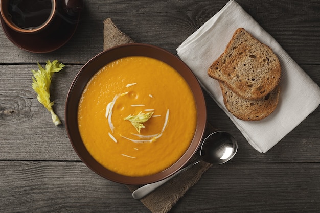 Sopa de abóbora com folhas de aipo e creme sobre uma mesa de madeira. Sopa De Creme De Abóbora De Outono Vegetariana. Vista do topo.