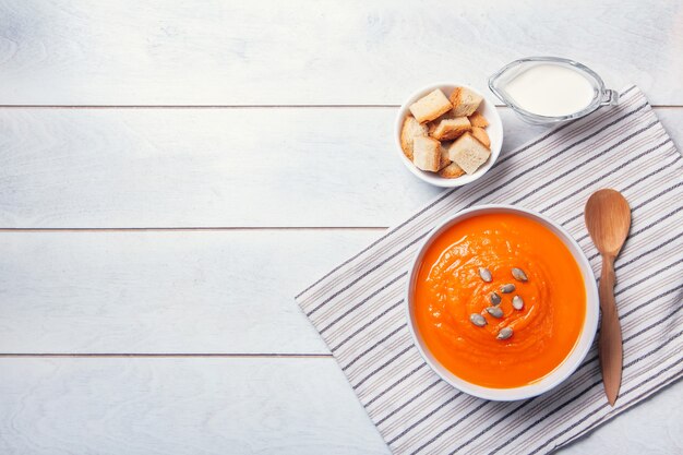 Sopa de abóbora com purê de pão ralado, creme e sementes em um fundo branco de madeira. Copie o espaço.