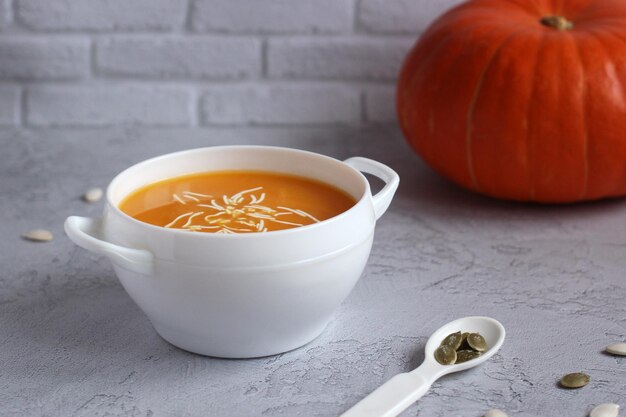 Sopa de abóbora com sementes de abóbora em uma tigela branca sobre um fundo cinza