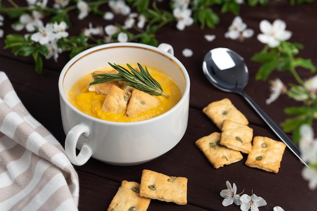 Sopa de abóbora cremosa orgânica picante fresca em tigela branca na mesa de madeira com biscoitos de pão