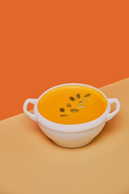 Foto sopa de abóbora decorada com sementes de abóbora isoladas em fundo laranja. monocromático, minimalismo. vista de cima. copie o espaço.