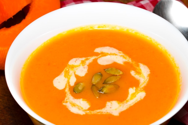 Foto sopa de abóbora e cenoura com creme e salsa no fundo escuro de madeira vista superior.