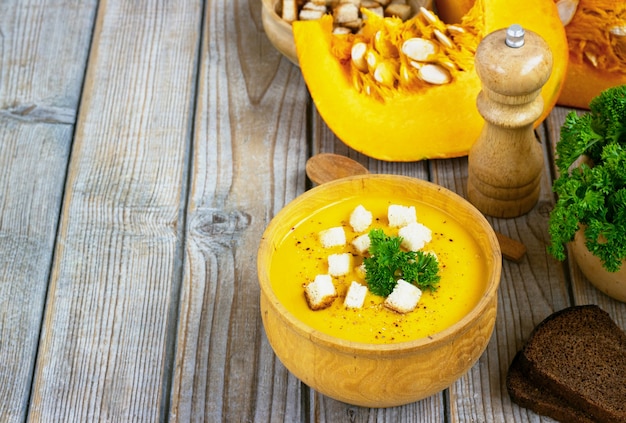 Sopa de abóbora e cenoura, tadka com creme e salsa na mesa de madeira escura. Vista do topo.