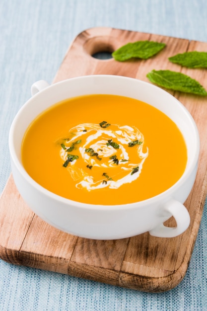 Sopa de abóbora em uma tigela branca na mesa azul