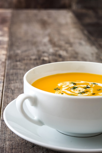 Sopa de abóbora em uma tigela branca na mesa de madeira