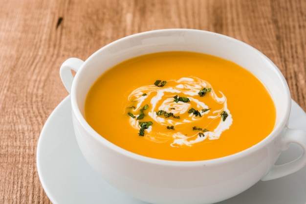 Sopa de abóbora em uma tigela branca na mesa de madeira