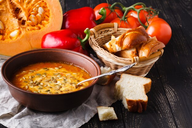 Sopa de abóbora em uma tigela na mesa rústica com pão