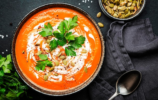 Sopa de abóbora picante de aquecimento de inverno com sementes creme de pimenta e salsa Conforto saudável comida lenta Tigela de sopa no fundo da mesa preta Vista superior