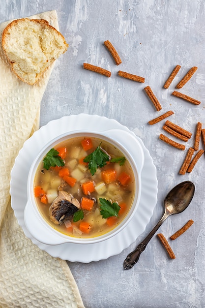 Foto sopa de atum com batatas e cenouras, sobre um fundo de concreto com verduras e bolachas