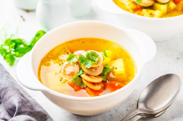 Sopa de batata alemão com salsichas e vegetais nas bacias brancas, fundo branco.