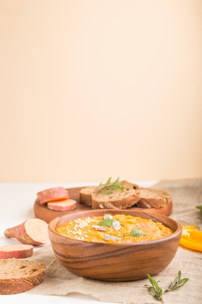 Sopa de batata doce ou creme de batata com sementes de gergelim em uma tigela de madeira em uma parede de madeira branca. Vista lateral, foco seletivo.