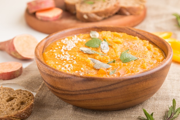 Sopa de batata doce ou creme de batata com sementes de gergelim em uma tigela de madeira em uma parede de madeira branca. Vista lateral, foco seletivo.