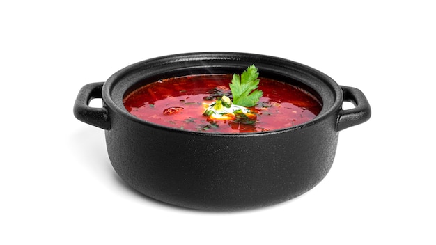 Sopa de beterraba vermelha quente - sopa de beterraba com creme de leite e ervas em uma panela preta isolada no branco.
