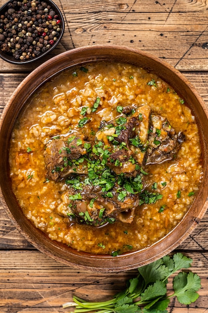 Sopa de carne de cordeiro georgian kharcho com arroz, tomate e especiarias em uma tigela de madeira. fundo de madeira. vista do topo.