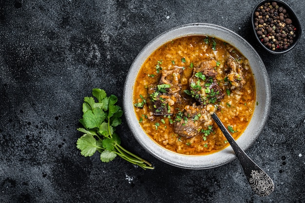 Sopa de cordeiro Kharcho com carne de carneiro, arroz, tomate e especiarias em uma tigela. Fundo preto. Vista do topo. Copie o espaço.