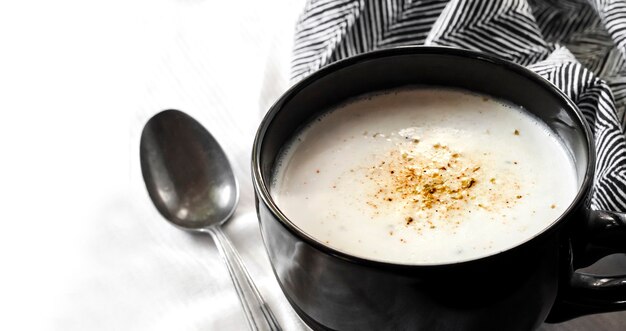 Sopa de couve-flor (Creme du Barry) em tigela preta sobre fundo branco com pano preto e branco com espaço de cópia