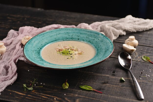 Sopa de creme com cogumelos. Em um prato azul em uma mesa de madeira com decoração