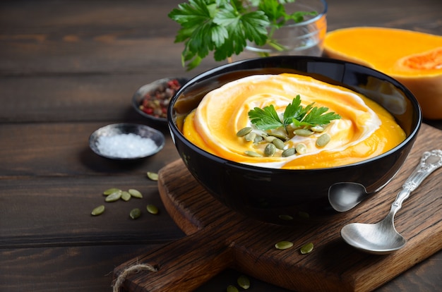 Sopa de creme de abóbora com creme e sementes de abóbora na mesa de madeira.