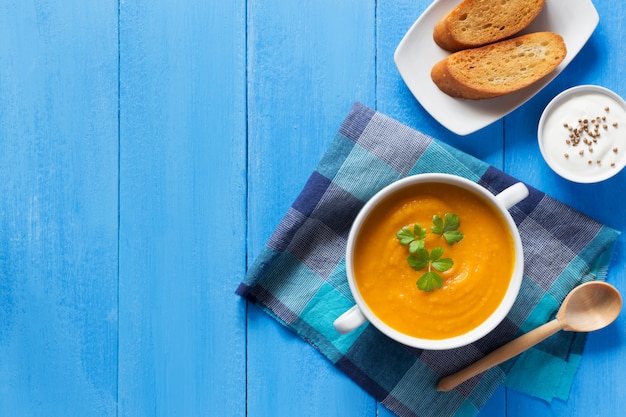 Sopa de creme de abóbora com pão na mesa azul