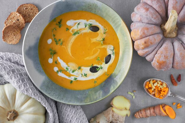 Sopa de creme de abóbora em uma tigela de cerâmica temperada com tomilho, creme e croutons, com abóbora, pimenta e curcuma fresca