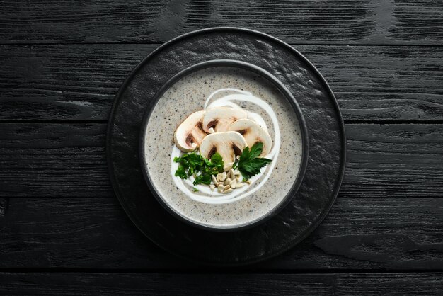 Sopa de creme de cogumelos em uma tigela preta. Cardápio vegetariano. Vista do topo. Espaço livre para o seu texto. Estilo rústico.