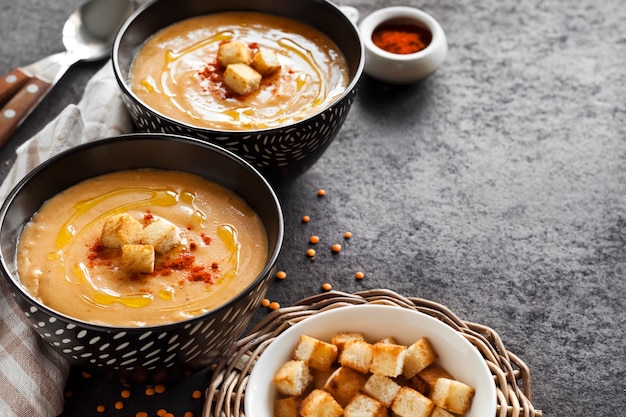 Sopa de creme de lentilha com páprica e pão torrado em tigelas de cerâmica preta sobre fundo escuro. Copie o espaço