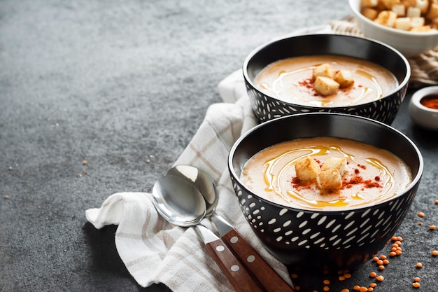 Sopa de creme de lentilha com páprica e pão torrado em tigelas de cerâmica preta sobre fundo escuro. Copie o espaço