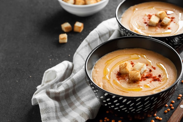 Sopa de creme de lentilha com páprica e pão torrado em tigelas de cerâmica preta sobre fundo escuro. Copie o espaço