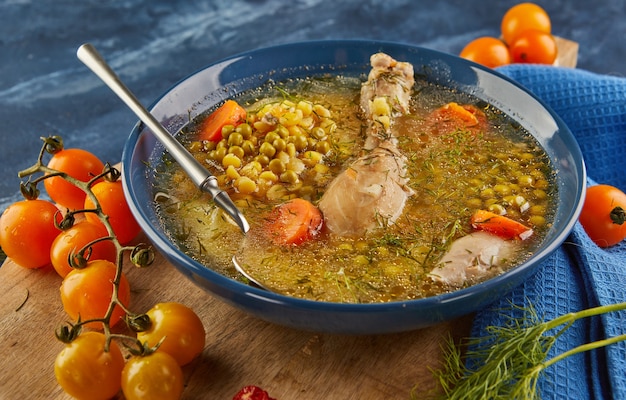 Sopa de ervilha com frango, cenoura, tomate e ervas em uma placa funda na placa de madeira com guardanapo.