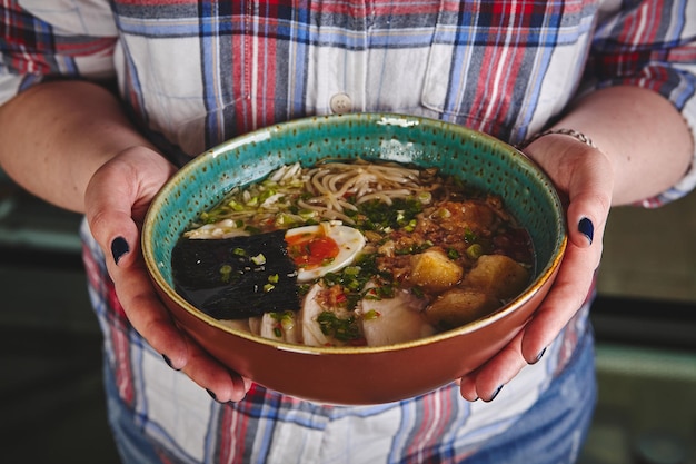 Sopa de estilo asiático com ovo de macarrão em tigela nas mãos de uma jovem