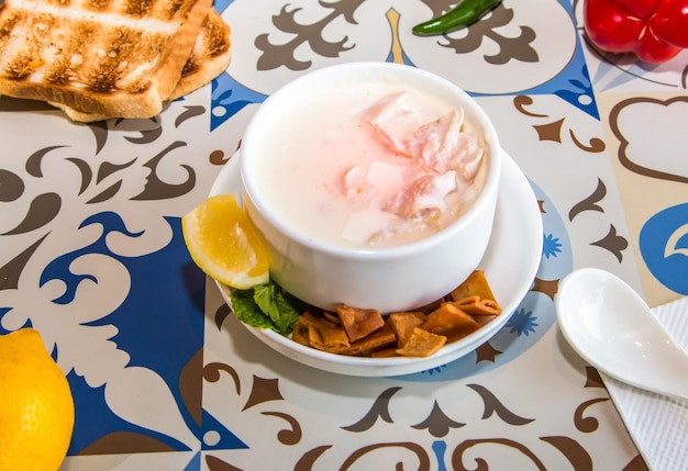 Sopa de frango com creme com biscoitos, pão de limão e colher servida em uma panela isolada na mesa, vista da comida árabe