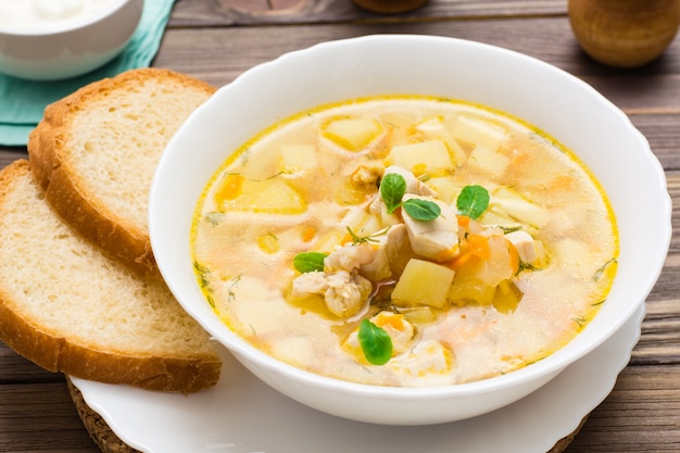 sopa de galinha com batatas e ervas em uma tigela branca em uma mesa de madeira