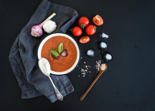 Sopa de gaspacho em tigela de metal rústica com tomates frescos cubos de gelo alho e manjericão sobre o pano de fundo grunge escuro