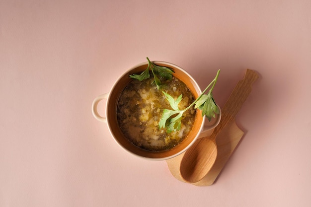 Foto sopa de legumes em um prato e colher sobre fundo rosa