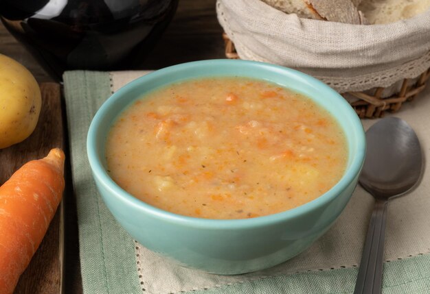 Sopa de legumes em uma tigela com fatias de pão e vinho sobre a mesa de madeira