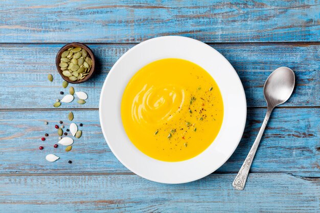 Sopa de legumes ou abóbora de outono com sementes em tigela branca na mesa de madeira turquesa vista superior