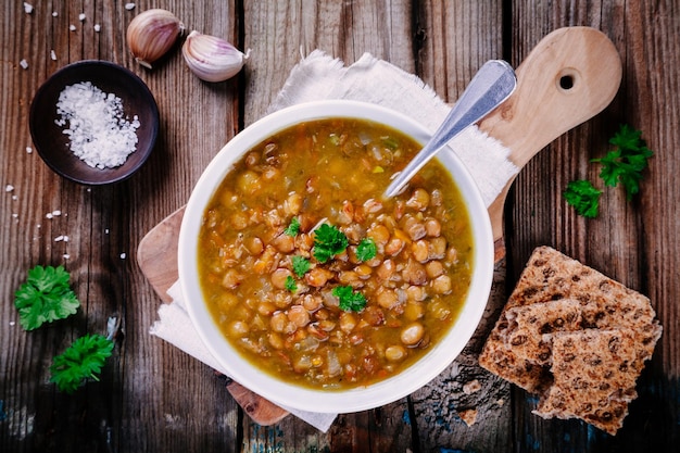 Sopa de lentilha com pão estaladiço e salsa na mesa de madeira