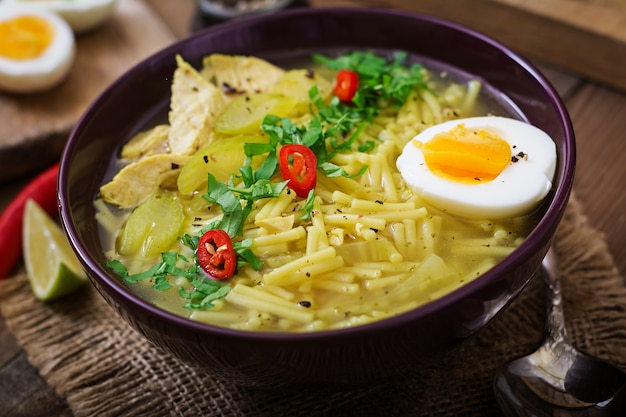 Sopa de macarrão com frango, aipo e ovo em uma tigela em um fundo de madeira velho.